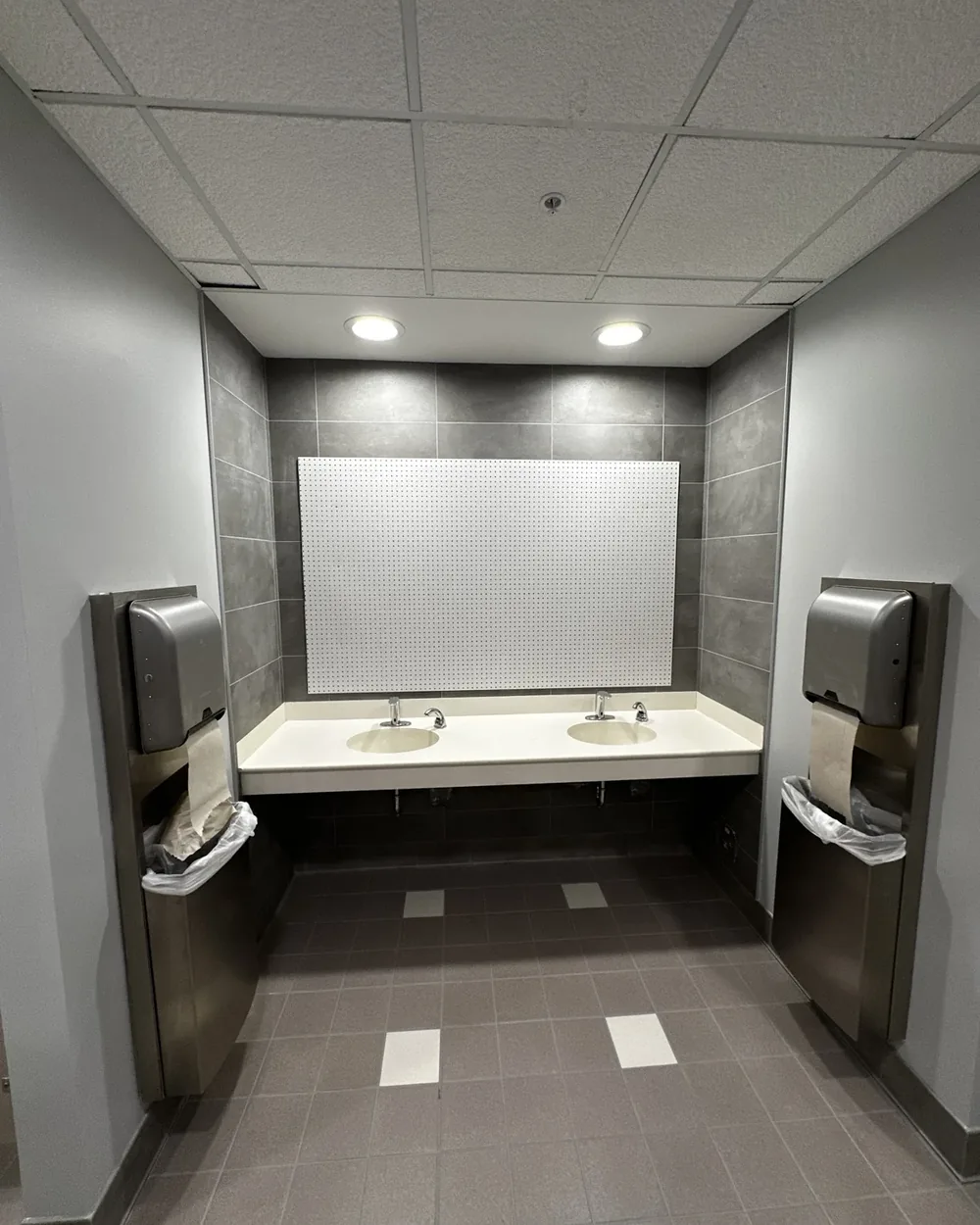 Finished commercial restroom with a solid-surface lavatory counter, mirror, and stainless wall-mounted accessories